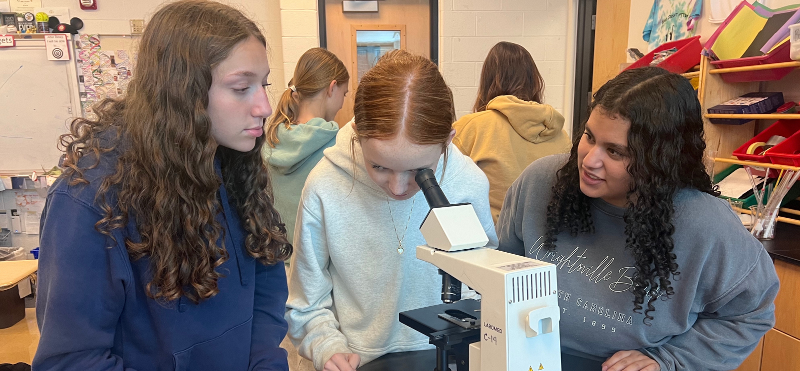 3 high school students looking in a microscope