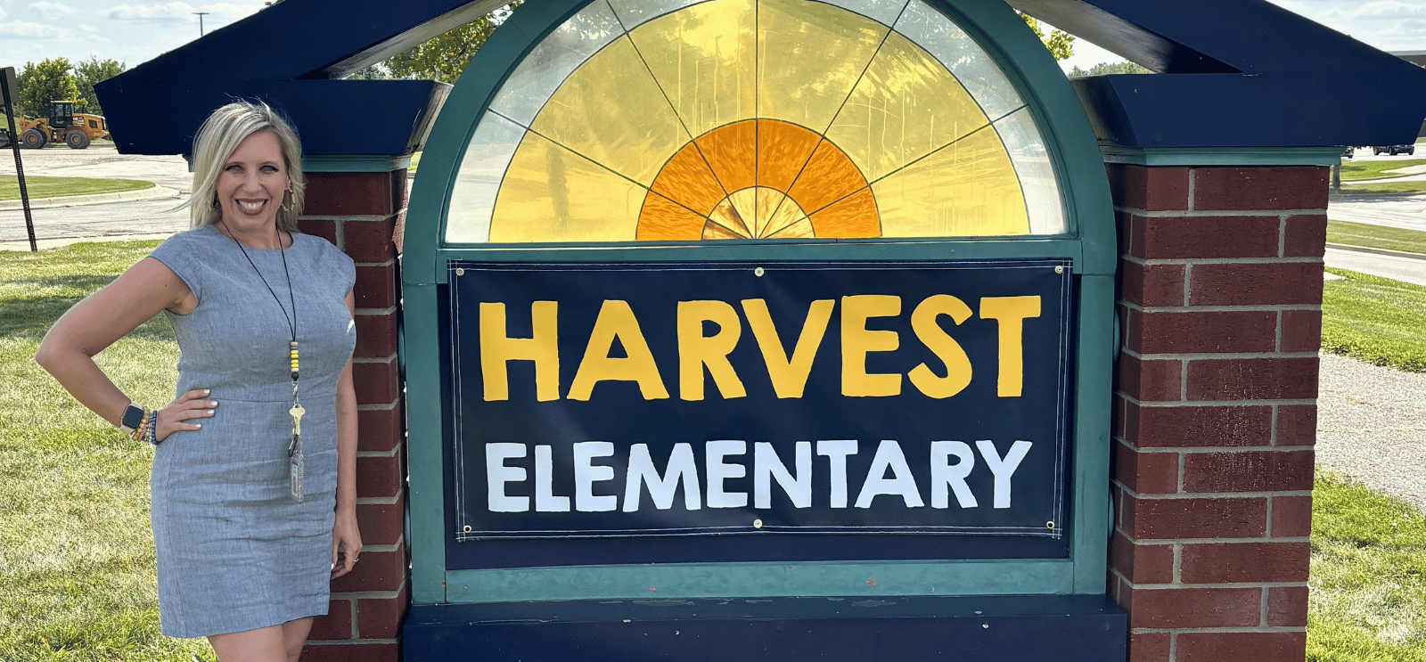 Principal Emily Sickler in front of Harvest Elementary sign